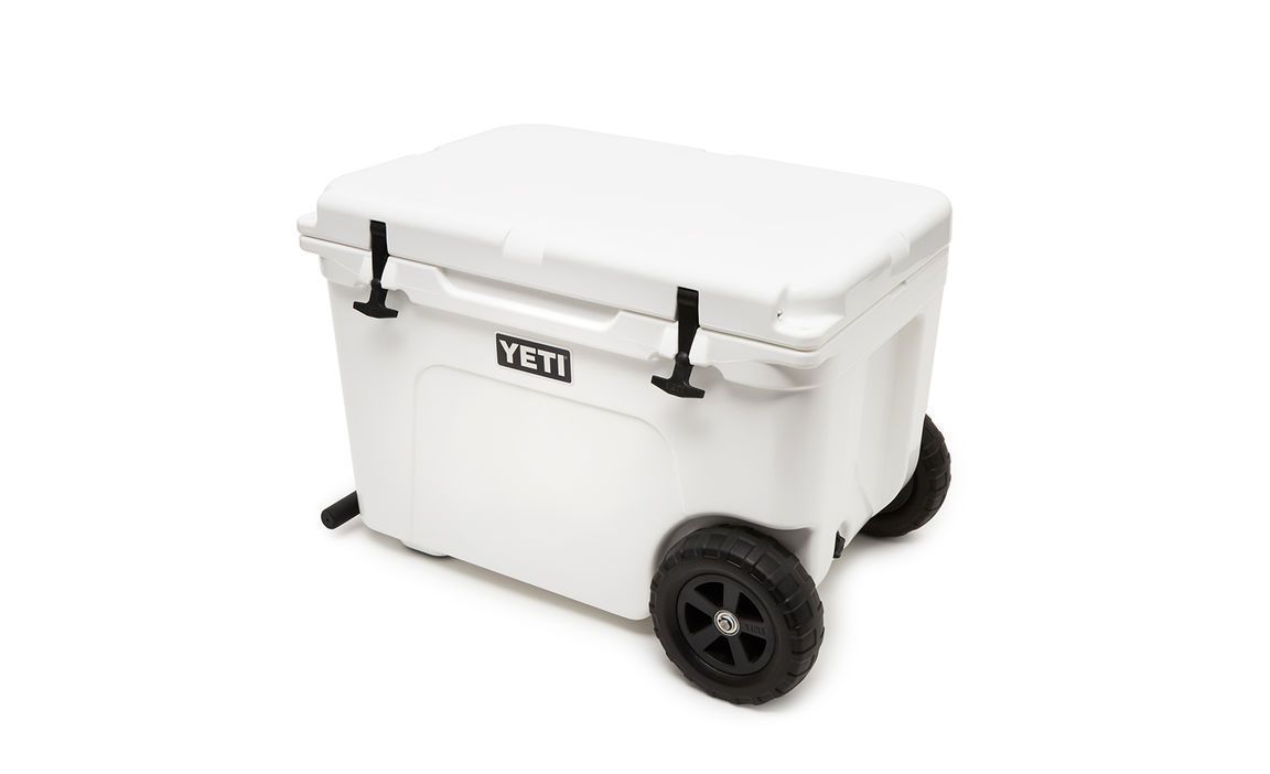 Die YETI® Kühlbox Tundra Haul - White verfügt über einen aufklappbaren Deckel, schwarze Griffe und große Räder für den einfachen Transport. Auf der Vorderseite ist das YETI-Logo abgebildet, was sie zur idealen Outdoor-Kühlbox macht.