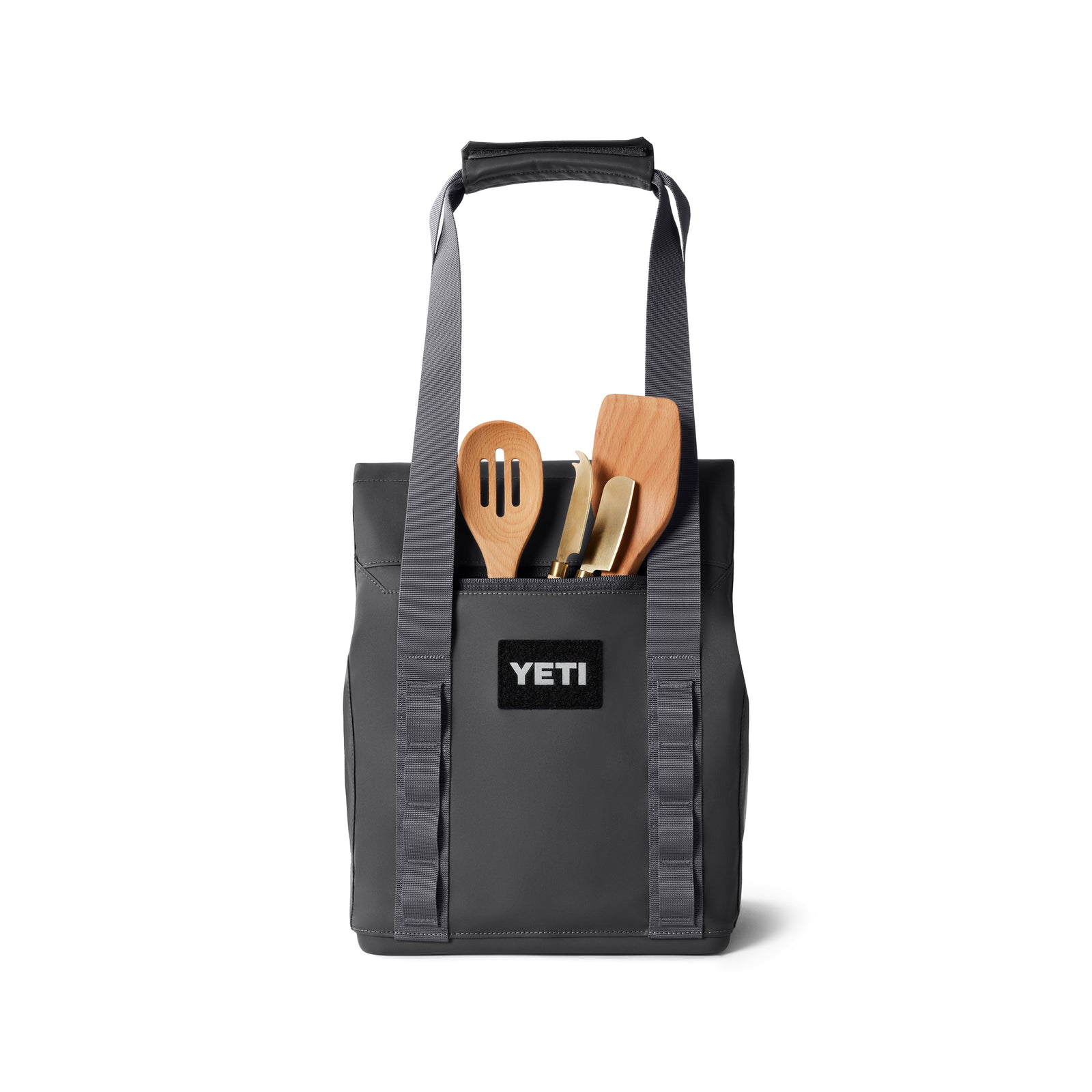 Eine YETI® Kühltasche Daytrip Lunch Bag 14L in Charcoal mit Griffen und Coldcell Flex Isolierung hält Holzkochutensilien und andere Küchenutensilien, alles aufrecht vor einem weißen Hintergrund.