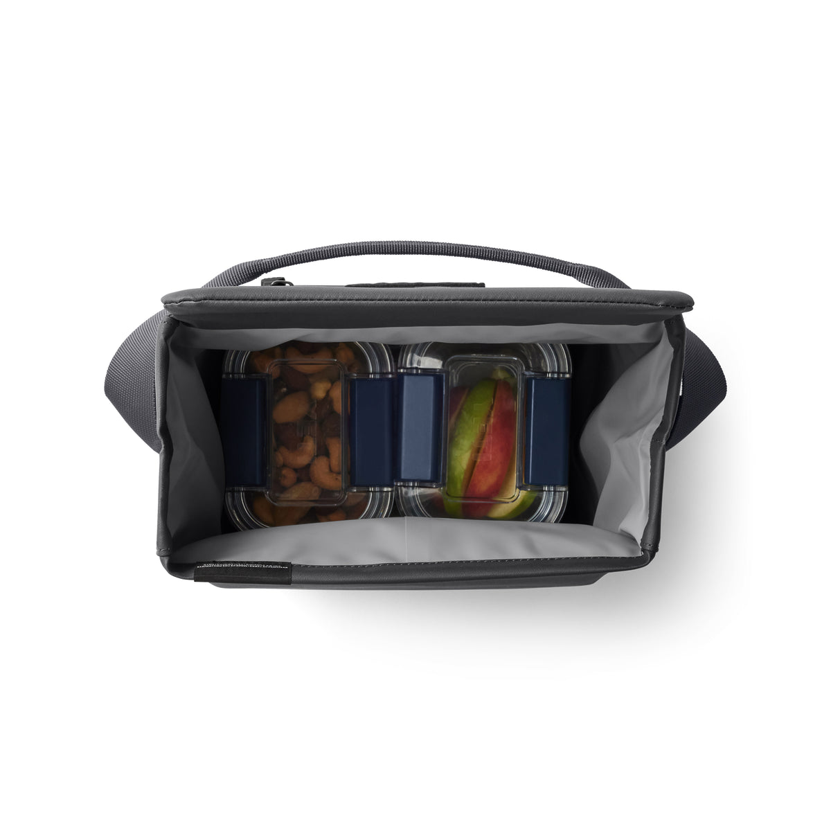 Draufsicht auf eine geöffnete YETI® Kühltasche Daytrip Lunch Bag 6L - Charcoal mit drei durchsichtigen Lebensmittelbehältern mit blauen Deckeln, gefüllt mit Nüssen und Fruchtscheiben, und einem leeren Behälter.