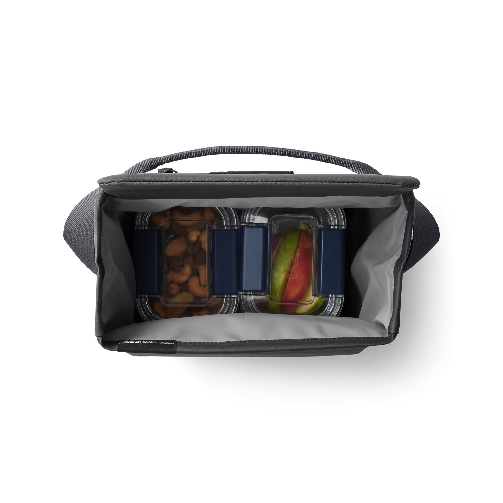 Draufsicht auf eine geöffnete YETI® Kühltasche Daytrip Lunch Bag 6L - Charcoal mit drei durchsichtigen Lebensmittelbehältern mit blauen Deckeln, gefüllt mit Nüssen und Fruchtscheiben, und einem leeren Behälter.