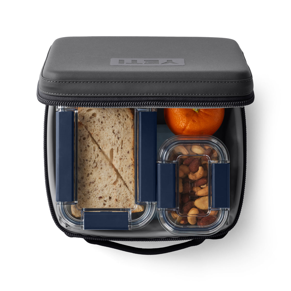 Eine Lunchbox mit einem Sandwich, einer kleinen Orange und gemischten Nüssen, alles verpackt in der YETI® Kühltasche Daytrip Lunch Box 3L - Charcoal für dauerhafte Frische.