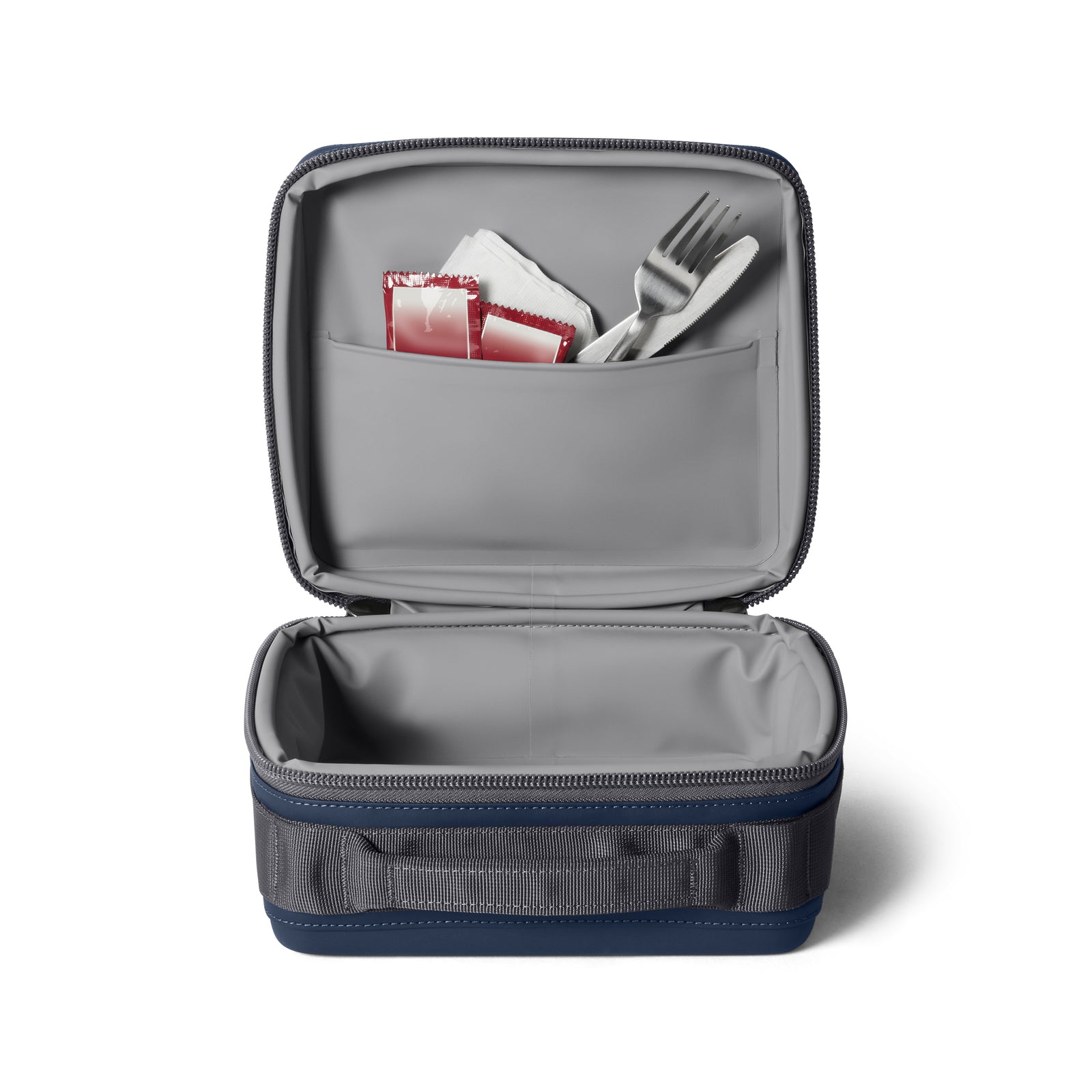 Die navyfarbene YETI® Kühltasche Daytrip Lunch Box 3L ist offen und zeigt in ihrem Innenfach eine Gabel und zwei Gewürzpakete, während das Hauptfach leer ist - ideal, um Lebensmittel durch zuverlässige Kühlung frisch zu halten.