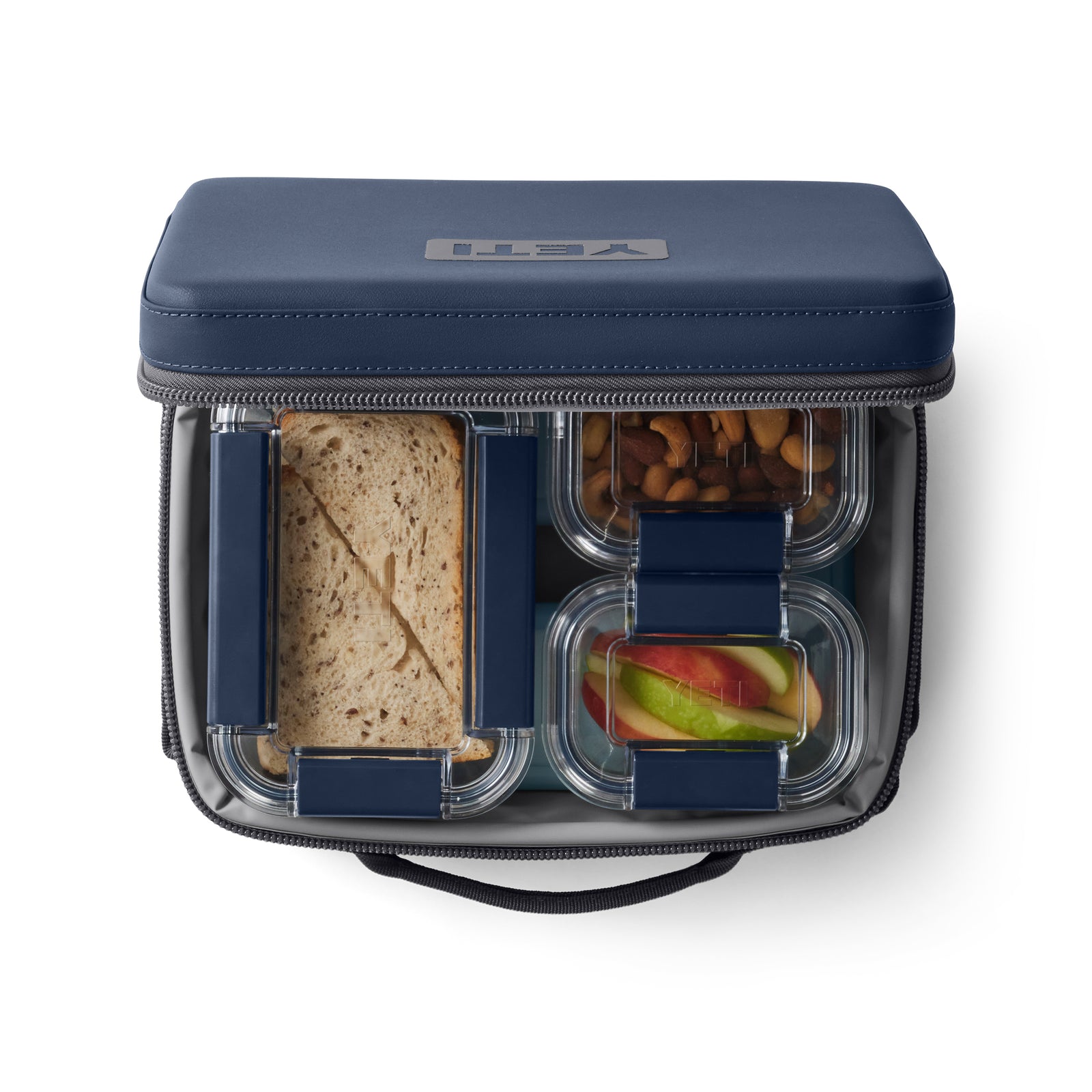 Die navyfarbene YETI® Kühltasche Daytrip Lunch Box 5L ist offen und gibt den Blick frei auf ein Sandwich, geschnittene Äpfel und Nüsse, die in durchsichtigen Behältern in dieser praktischen Lunchbox von YETI aufbewahrt werden.