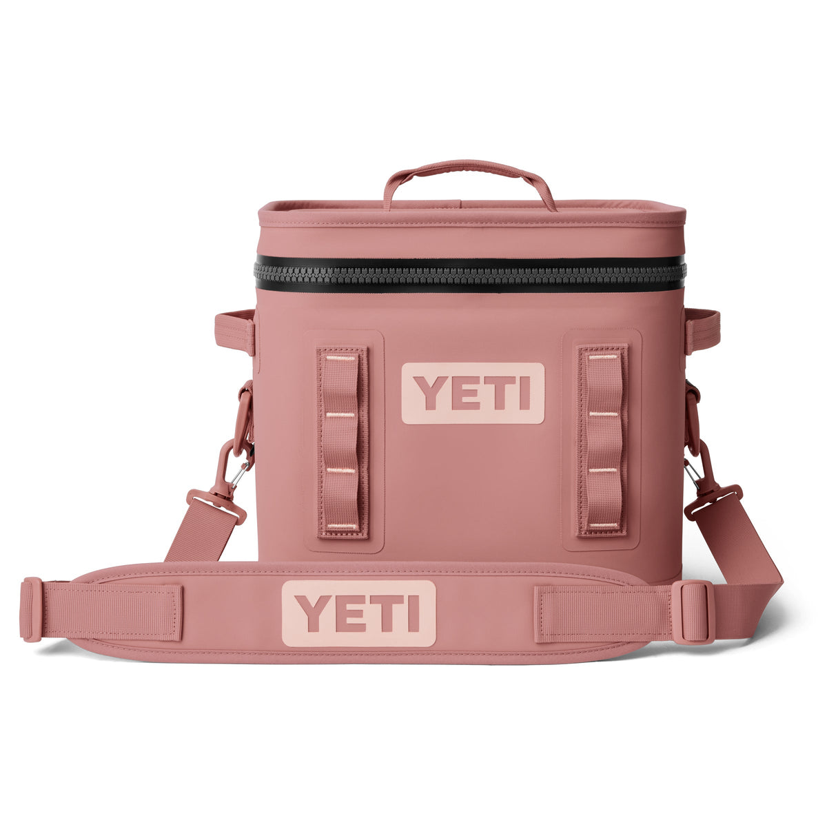Die YETI® Kühltasche Hopper Flip® 12 in Sandstone Pink verfügt über einen Griff an der Oberseite, einen verstellbaren Schultergurt, einen Deckel mit Reißverschluss und zwei YETI-Logos auf der Vorderseite und dem Gurt, die auf weißem Hintergrund abgebildet sind.