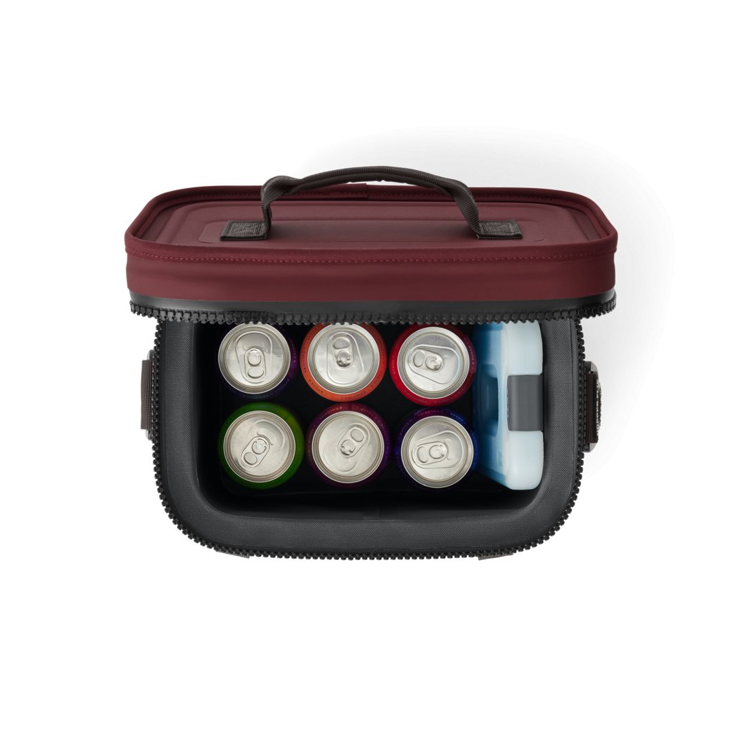 Draufsicht auf eine geöffnete YETI® Kühltasche Hopper Flip® 8 in Wild Vine Red, gefüllt mit sechs verschiedenen Getränkedosen und einem Eisbeutel, mit Reißverschluss und Tragegriff.