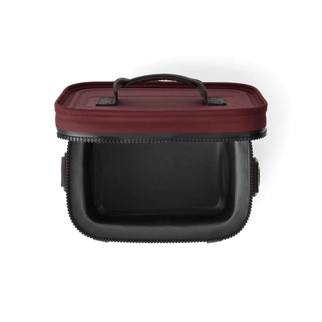 Eine rechteckige, schwarze YETI® Kühltasche Hopper Flip® 8 - Wild Vine Red mit kastanienbraunem Deckel, geöffnet mit halbem Reißverschluss und Griff, ist von oben auf einem weißen Hintergrund fotografiert.