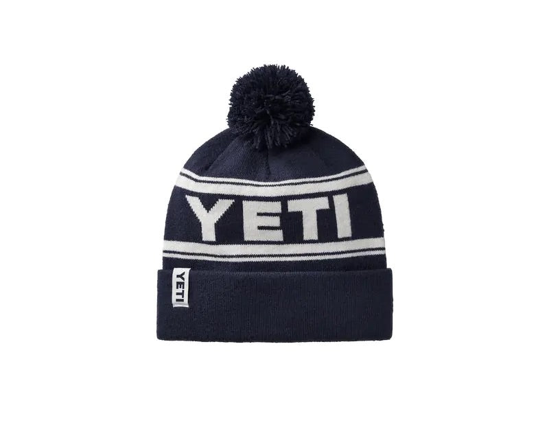 Die YETI® Logo Retro Knit Beanie ist marineblau und hat einen großen Bommel, einen auffälligen weißen "YETI"-Schriftzug, Retro-Streifen und eine umgeschlagene Krempe - perfekt für Fans des klassischen YETI-Stils.