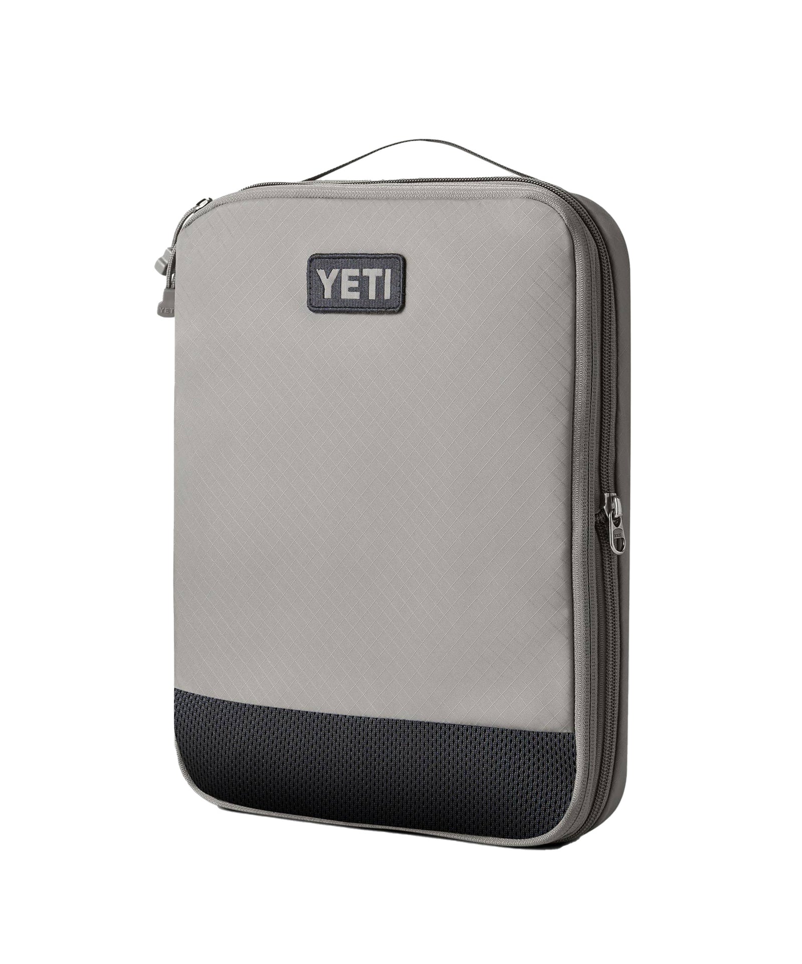 Die rechteckige, hellgraue YETI® Packtasche - Crossroads Cubes L hat einen schwarzen, strukturierten Boden, einen Reißverschluss am Rand, einen Tragegriff oben und das YETI-Logo auf der Vorderseite.