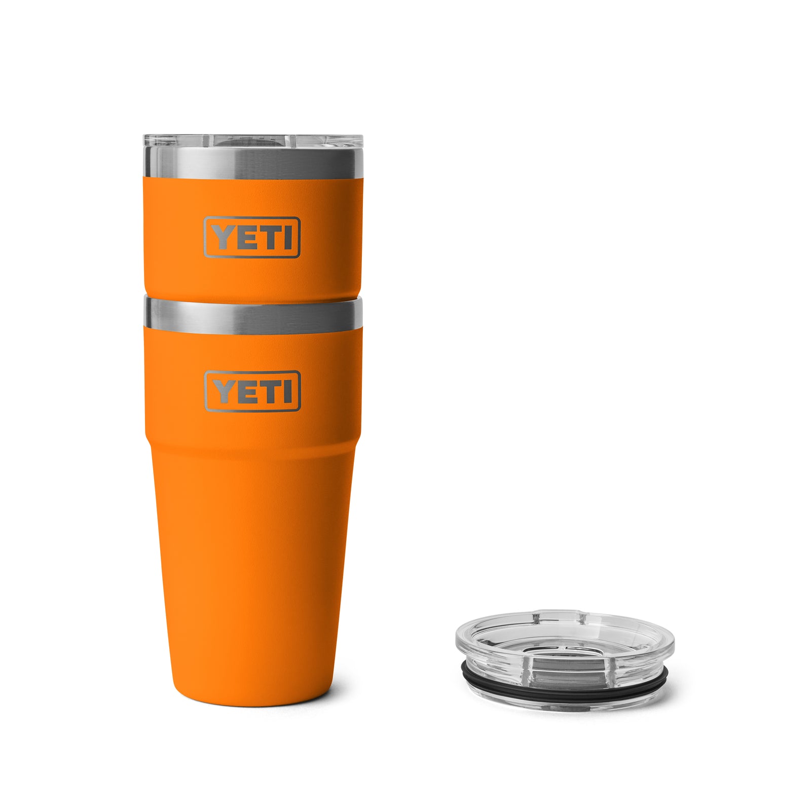 Zwei orangefarbene YETI® Rambler 20 Oz Stapelbarer Becher - King Crab sind auf der linken Seite gestapelt, mit einem separaten transparenten Deckel auf der rechten Seite vor einem weißen Hintergrund - mit doppelwandiger Vakuumisolierung.