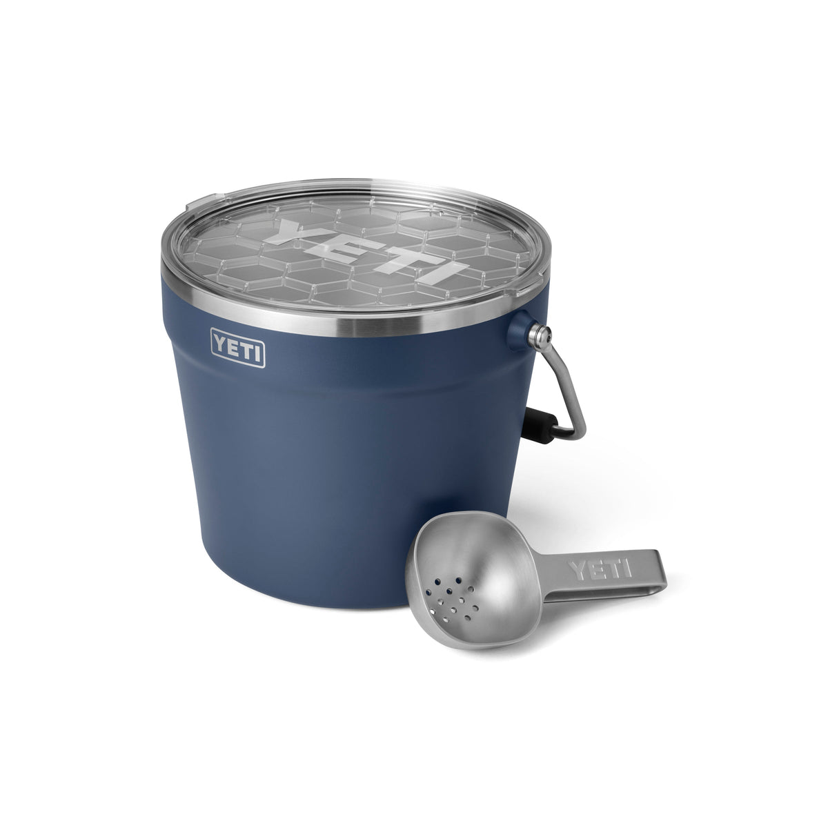 Ein YETI® Rambler® 7,6 Liter Getränkekübel in Navy mit doppelwandiger Vakuumisolierung und durchsichtigem Deckel steht neben einer silbernen Metallschaufel, beide auf weißem Hintergrund.