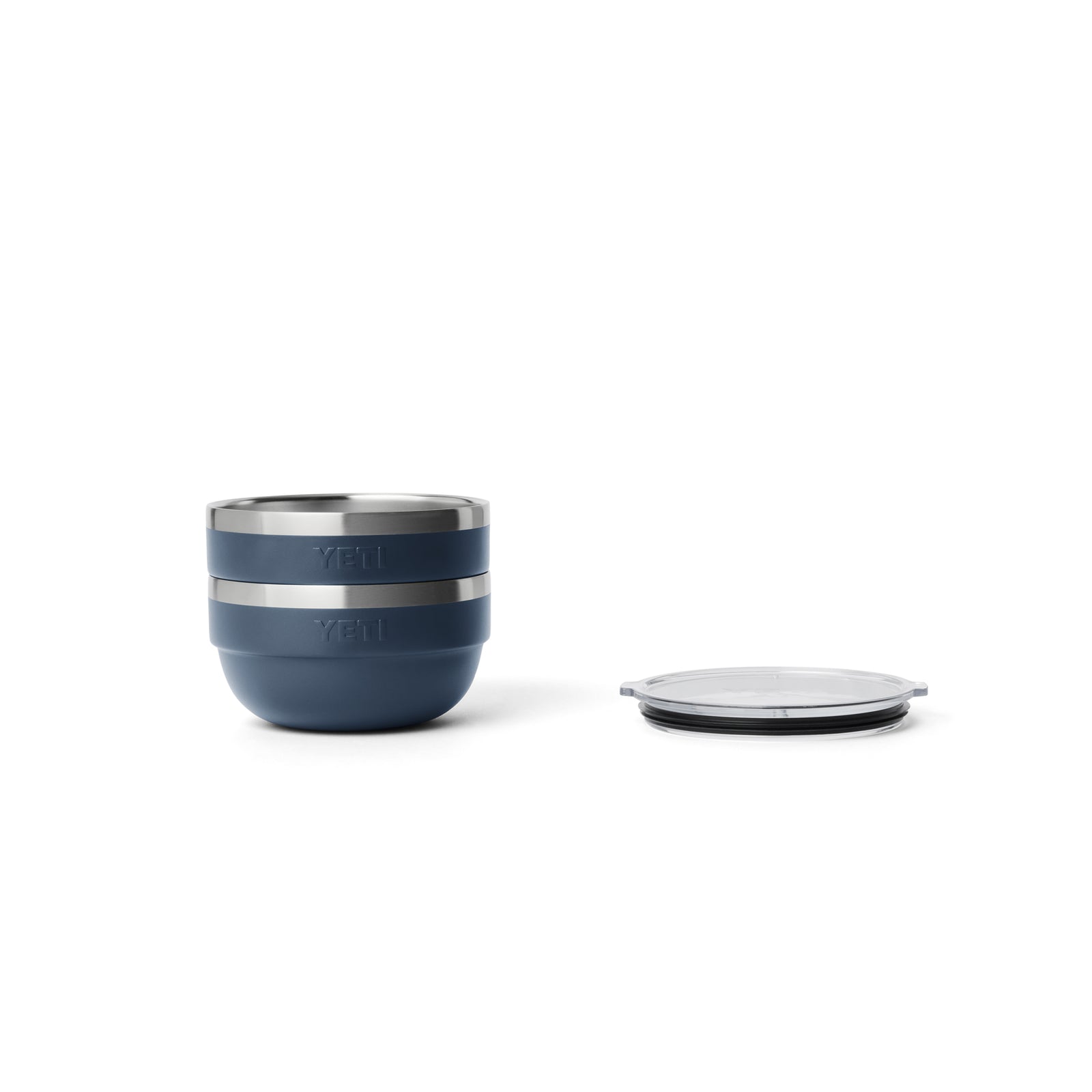 Eine YETI® Rambler Bowl Small - Navy von YETI mit zwei stapelbaren Schalen in Marineblau und Silber mit doppelwandiger Vakuumisolierung ist auf weißem Hintergrund abgebildet, wobei der durchsichtige Deckel separat rechts platziert ist.