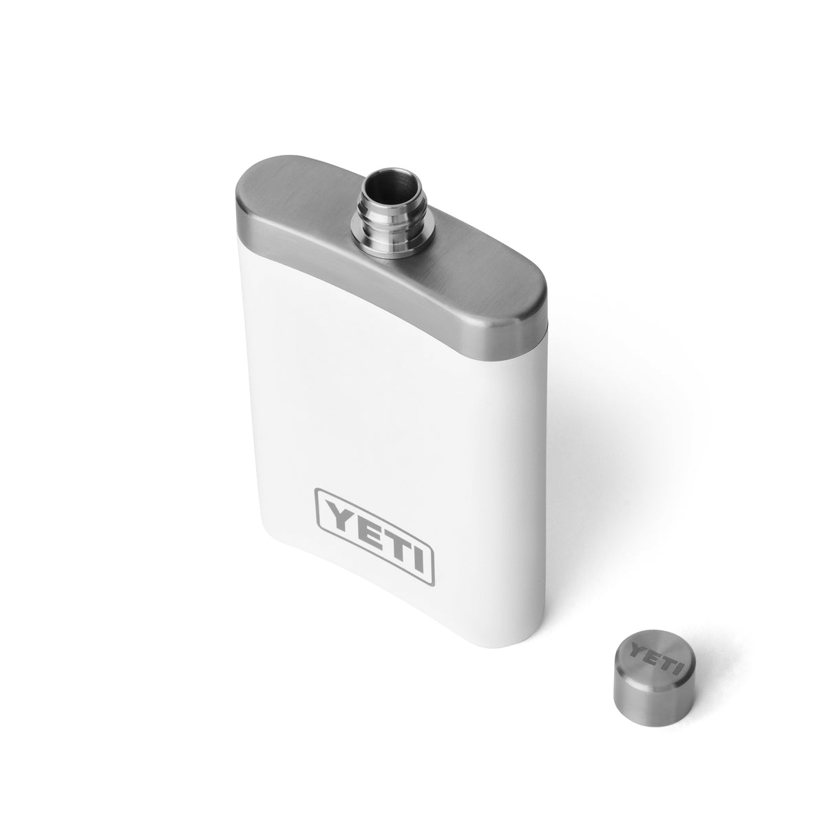 An der Seite befindet sich eine weiße YETI® Rambler Flask aus robustem 18/8-Edelstahl mit einem metallischen Schraubverschluss, auf dem das YETI-Logo eingeprägt ist, und einem sichtbaren YETI-Logo auf der Vorderseite.