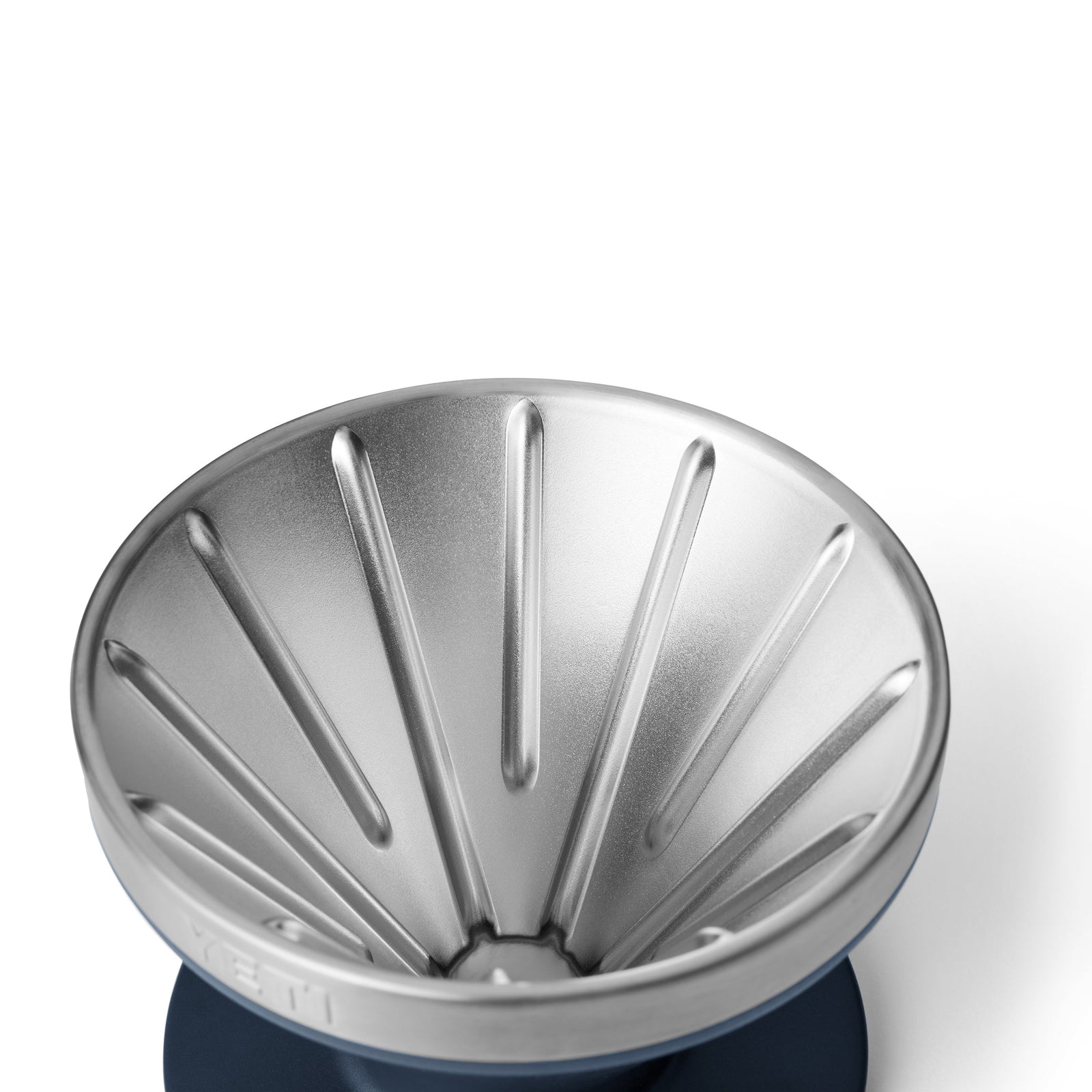 Eine Nahaufnahme eines YETI® Rambler Pour Over-Kaffeebereiter von YETI mit vertikalen Rillen, montiert auf einem marineblauen Sockel, vor einem weißen Hintergrund.