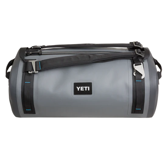 Die YETI® Reisetasche Panga 50 in Storm Grey verfügt über schwarze Riemen, blaue Nähte, einen oberen Reißverschluss und ein zentrales YETI-Logo - perfekt als wasserdichte Ausrüstungstasche für Ihr nächstes Abenteuer.