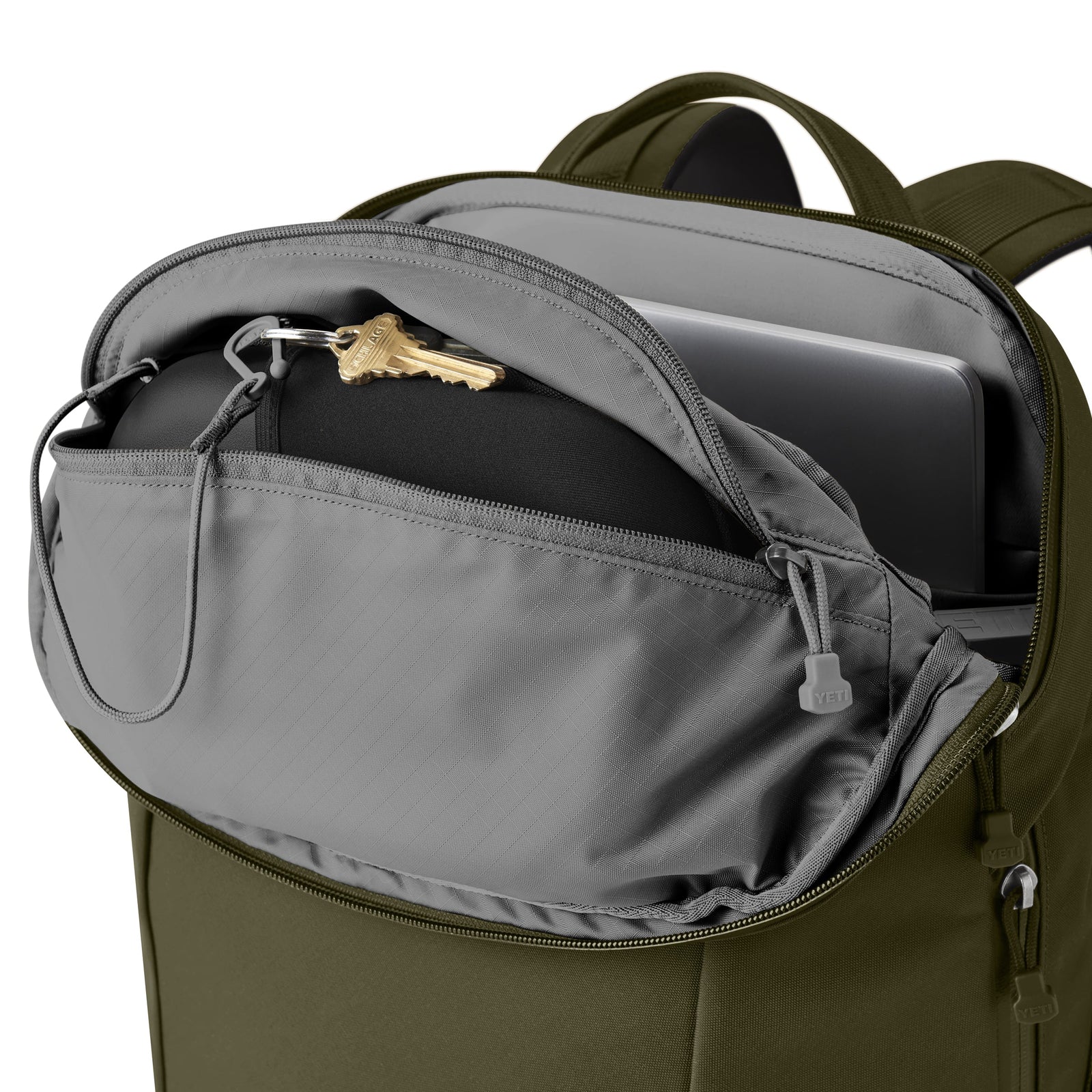 Der YETI® Rucksack Crossroads® 22L in Oliv mit grauem Innenraum ist geöffnet und zeigt einen Laptop, eine schwarze Tasche und Schlüssel in seinem Inneren - ein robuster Tagesrucksack von YETI für Ihre täglichen Essentials.