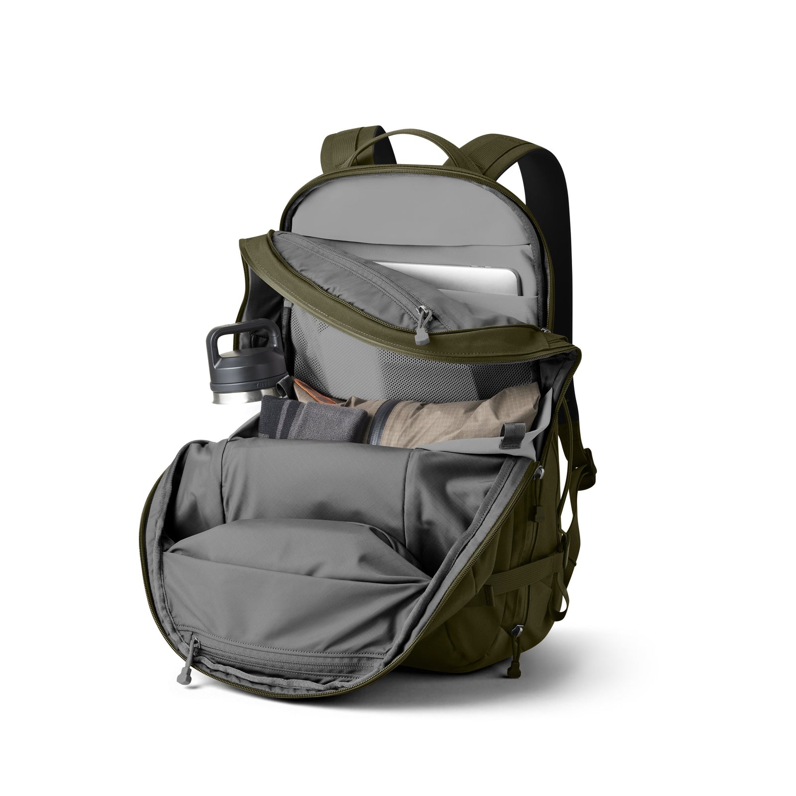 Der YETI® Rucksack Crossroads® 27L - Olive ist ohne Reißverschluss abgebildet, mit organisierten Gegenständen im Inneren wie Wasserflasche, Laptop, Notebook und ordentlich verpackter Kleidung.