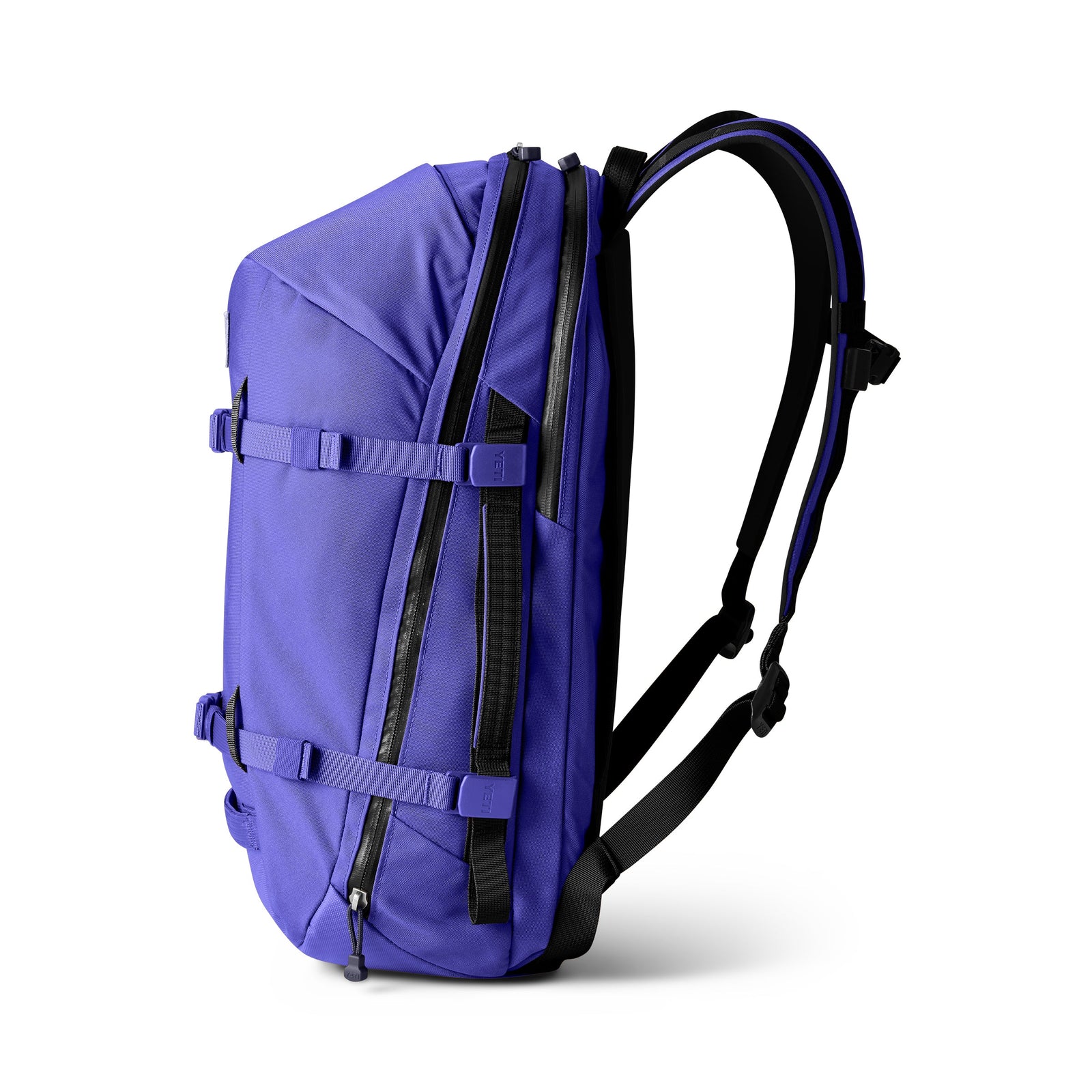 Der YETI® Rucksack Crossroads® 27L in Ultramarine ist von der Seite mit schwarzen gepolsterten Schultergurten, Kompressionsriemen, Reißverschlussfächern und Schnallenverschlüssen vor weißem Hintergrund dargestellt.