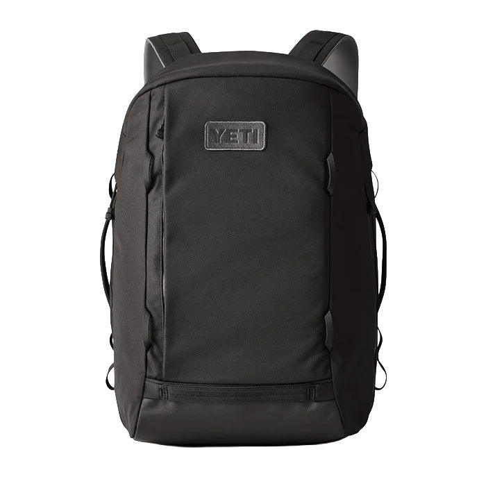 Der YETI® Rucksack Crossroads® 35L in Schwarz mit gepolsterten Schultergurten, Frontreißverschluss, Seitentaschen und einem Laptopfach ist auf weißem Hintergrund mit dem YETI-Logoaufnäher oben in der Mitte abgebildet.