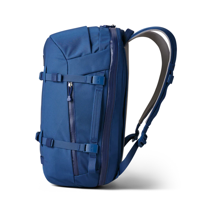 Der YETI® Rucksack Crossroads® 35L in Navy von YETI verfügt über gepolsterte Schultergurte, eine Fronttasche mit Reißverschluss und verstellbare Kompressionsriemen. Abgebildet ist er angewinkelt vor einem weißen Hintergrund.
