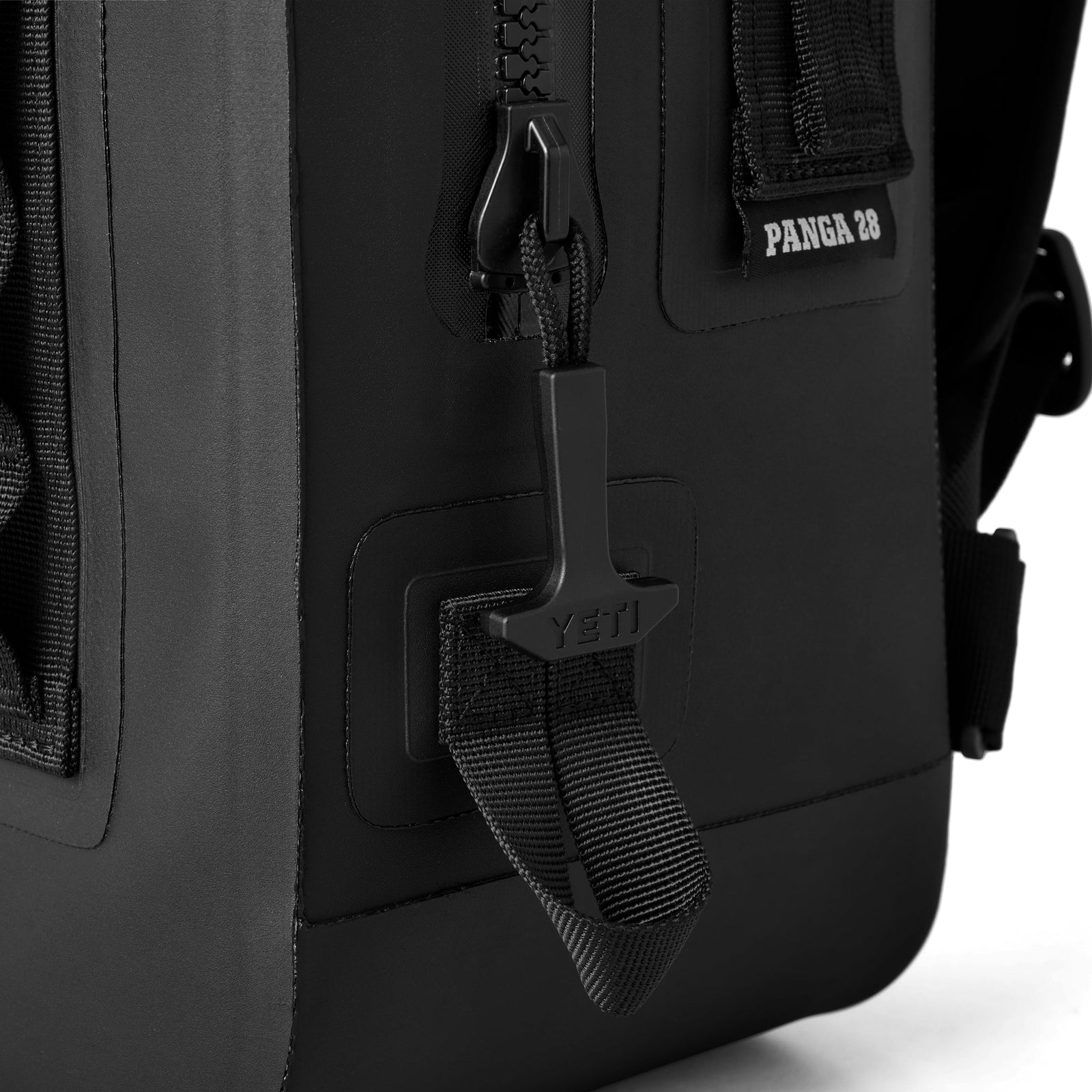 Nahaufnahme des schwarzen YETI® Rucksack Panga 28 mit robustem Reißverschluss, großer Zuglasche und Riemen. Das Etikett PANGA 28 in der Nähe des Reißverschlusses weist auf das robuste Design dieses wasserdichten Rucksacks von YETI hin.