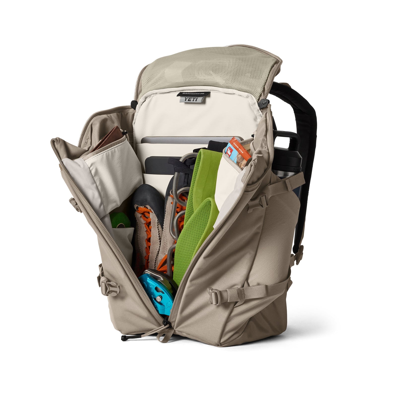 Ein YETI® Rucksack Ranchero™ 22L in Cape Dark Taupe wird aufgeklappt und zeigt ein Laptopfach und die Wanderausrüstung - Kletterschuhe, Helm, grüne Matte, Seil, Wasserflasche und Ausweis -, die alle ordentlich an ihren vorgesehenen Plätzen angeordnet sind.