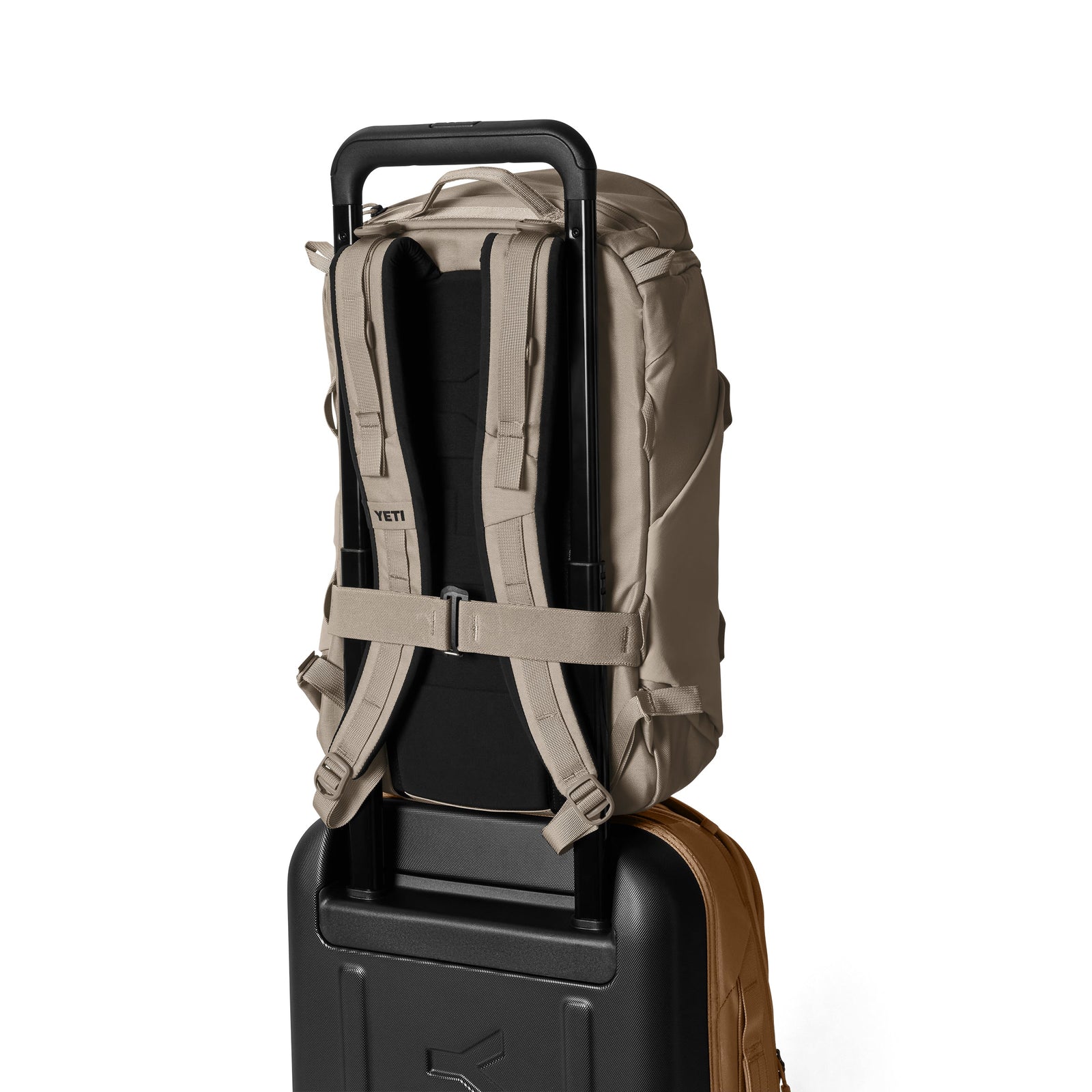Rückansicht des YETI® Rucksack Ranchero™ 22L in Cape Dark Taupe, der über die Gepäckhülle an einem schwarzen Rollkoffer befestigt ist, zeigt gepolsterte Schultergurte, einen Brustgurt und ein praktisches Laptopfach vor weißem Hintergrund.