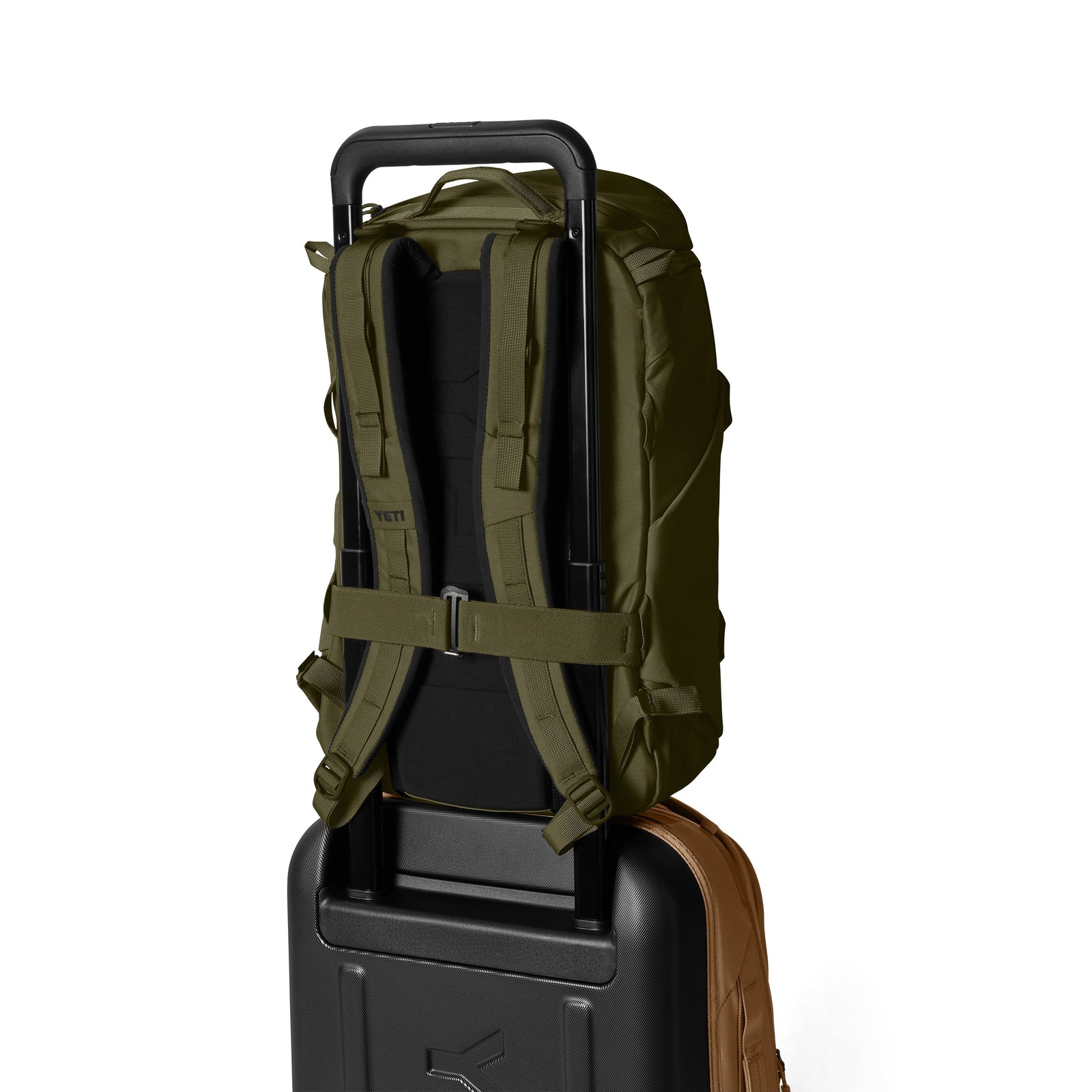 Ein YETI® Rucksack Ranchero™ 22L - Olive mit Laptopfach und gepolsterten Schultergurten ruht auf einem schwarzen Rollkoffer mit ausgezogenem Griff, beide vor einem schlichten weißen Hintergrund.