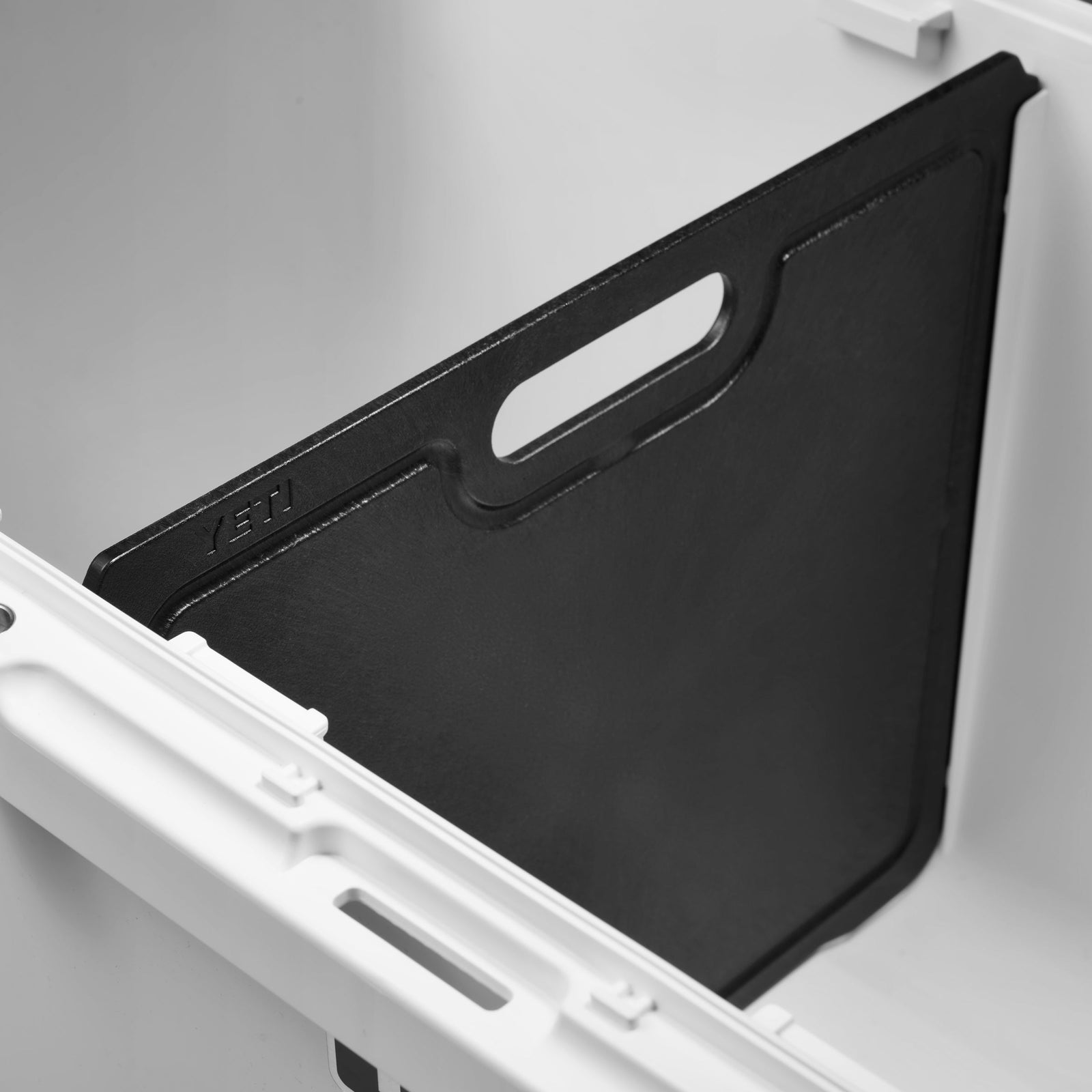 Eine Nahaufnahme der schwarzen YETI® Trennwand zu LoadOut GoBox 60 zeigt sie aufrecht mit ihrem Griffschlitz, gesichert durch die geriffelten Seiten der weißen GoBox 60-Kühlbox für eine stabile Organisation als Teil des YETI-Zubehörsortiments.