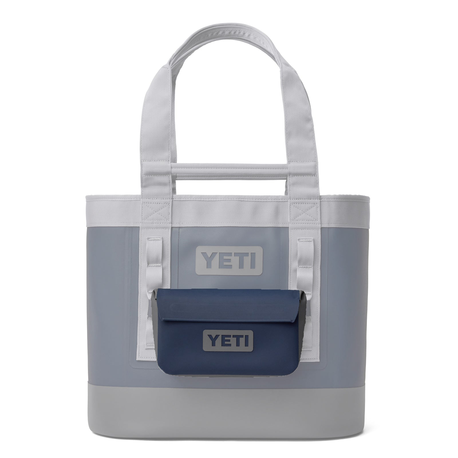 Eine grau-weiße YETI-Tasche mit robusten Griffen trägt auf der Vorderseite die marinefarbene YETI® Zubehörtasche - Sidekick® 1L. Beide Taschen sind mit einem auffälligen YETI-Branding versehen - ideal für Outdoor-Abenteuer und um die Ausrüstung trocken zu halten.